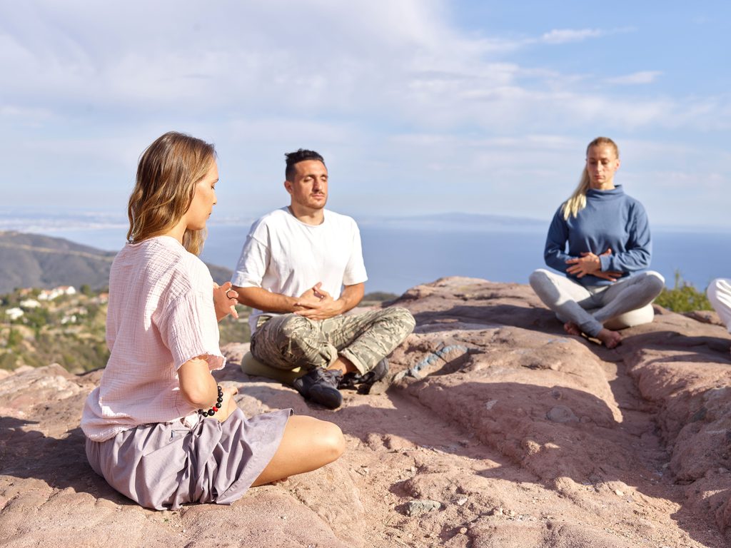 People practicing mindfulness meditation outdoors on a mountain overlooking the sea