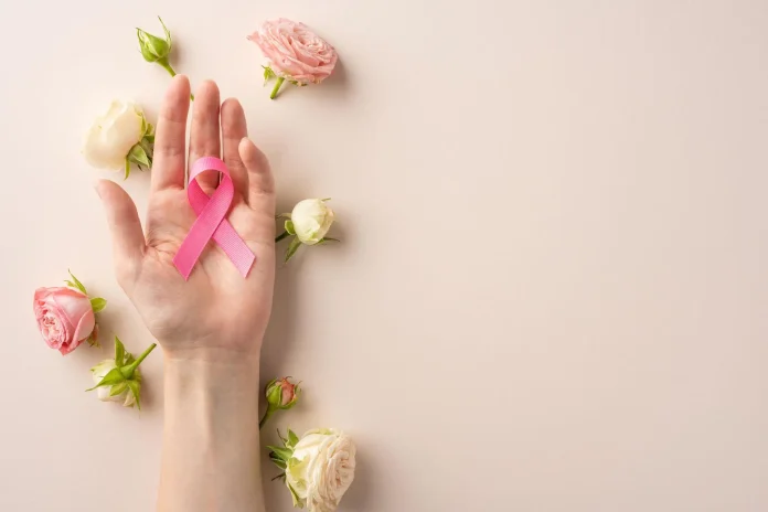 Pink breast cancer awareness ribbon held in a hand with pink and white flowers